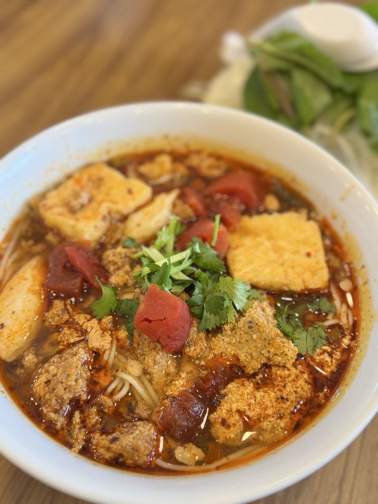 A bowl of bun rieu crab noodle soup with tomato, tofu, crab meat, and fresh herbs