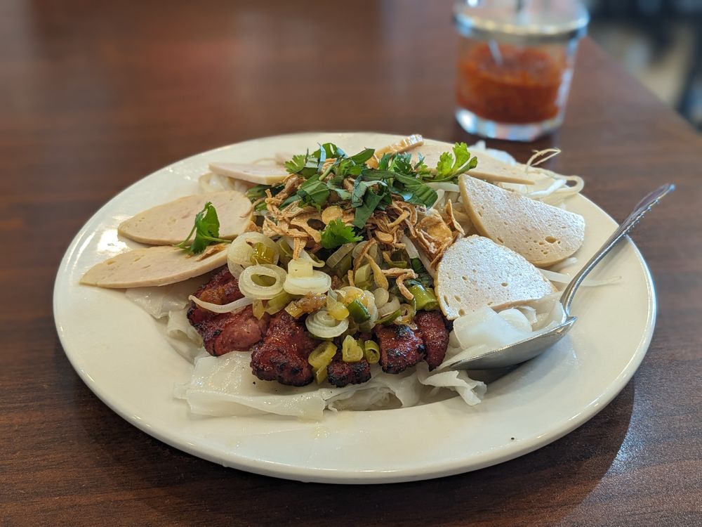 Steamed rice sheets with grilled pork, sliced cha lua, fried shallots, and fresh herbs