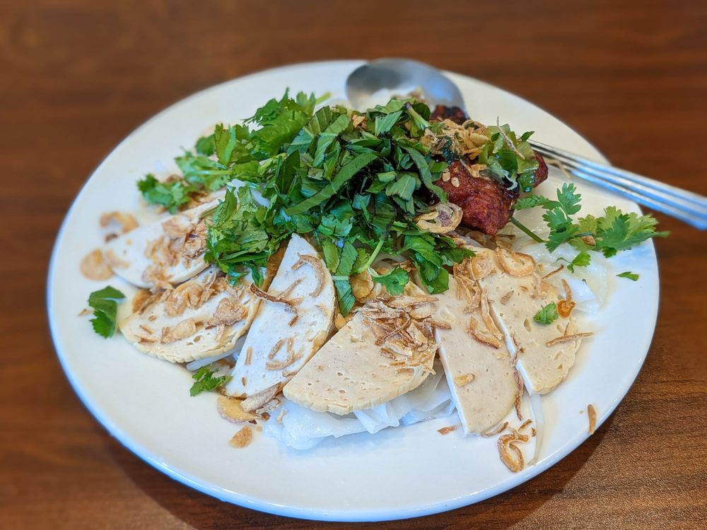 Steamed rice sheets topped with grilled pork, cha lua slices, fried shallots, and fresh herbs